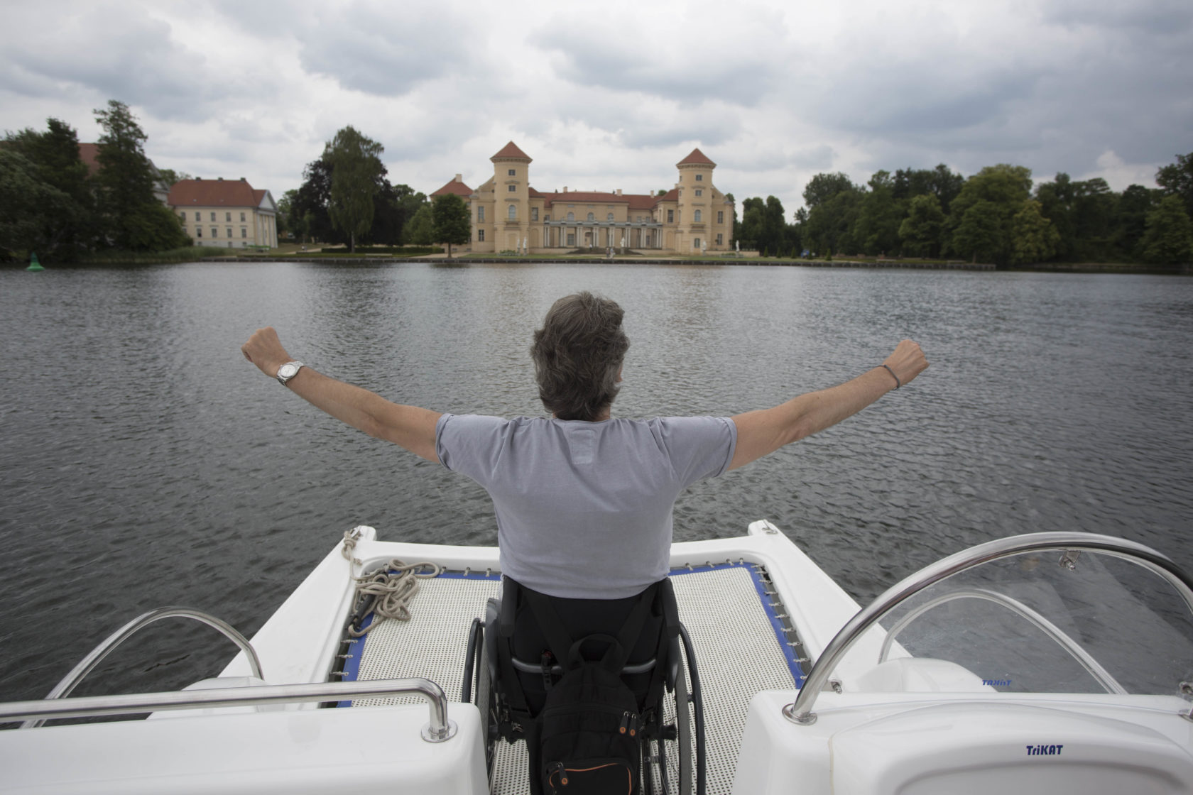 Ein Rollstuhlfahrer auf einem kleinen Boot erfreut sich über den Blick auf das Schloss Rheinsberg.