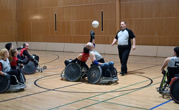 Zwei Rollstuhlbasketballspieler ringen um den Ball. Ein Schietsrichter beobachtet die Situation