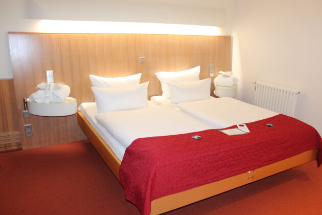Großzügiges Doppelbett in einem Hotelzimmer mit Bademantel auf dem Nachttisch